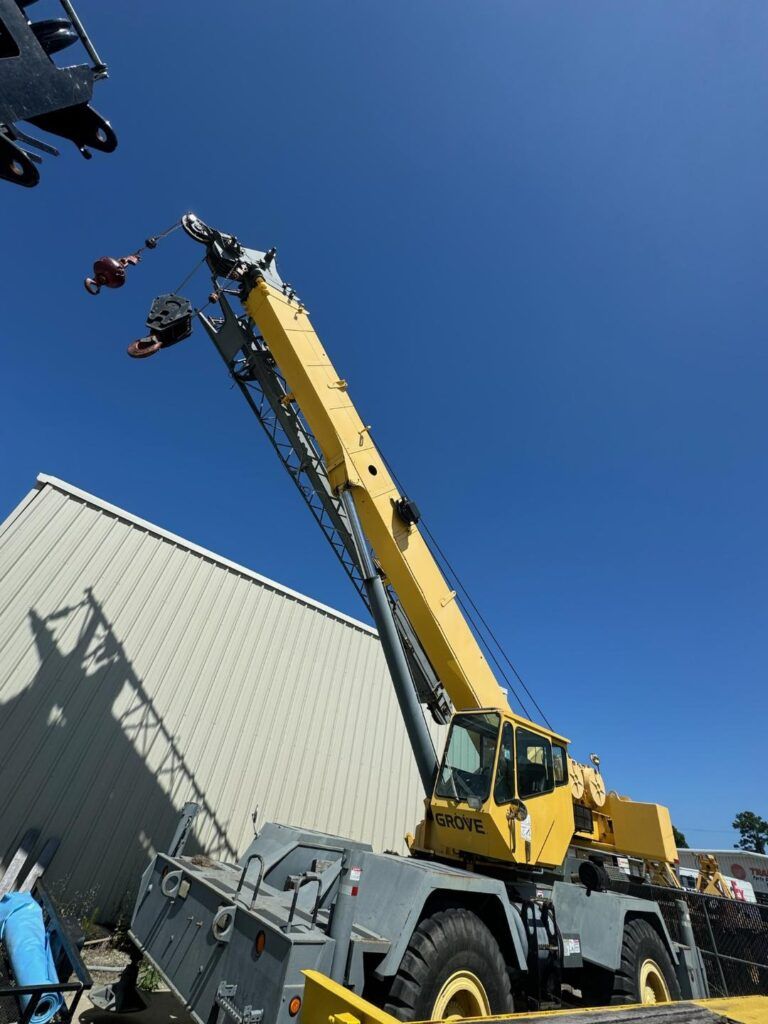 Yellow crane lifting equipment beside a warehouse under a clear blue sky