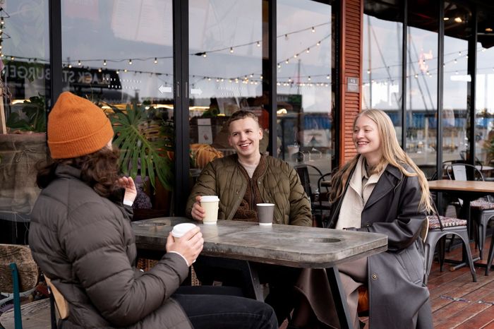 Three people chatting at an outdoor café table with coffee cups