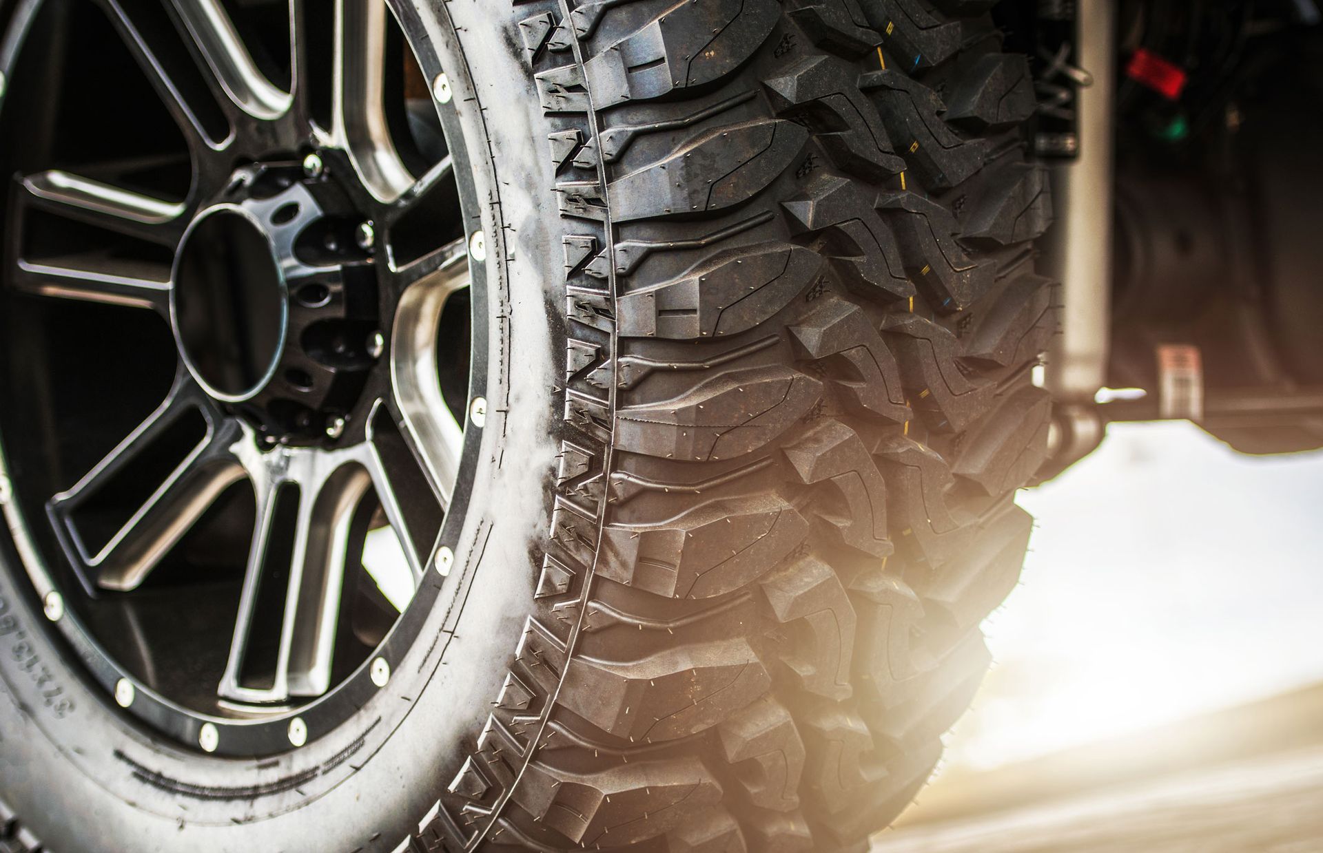 Close-up of a rugged black tire and rim, partially lit by sunlight. Close-up of a rugged black tire and rim, partially lit by sunlight.