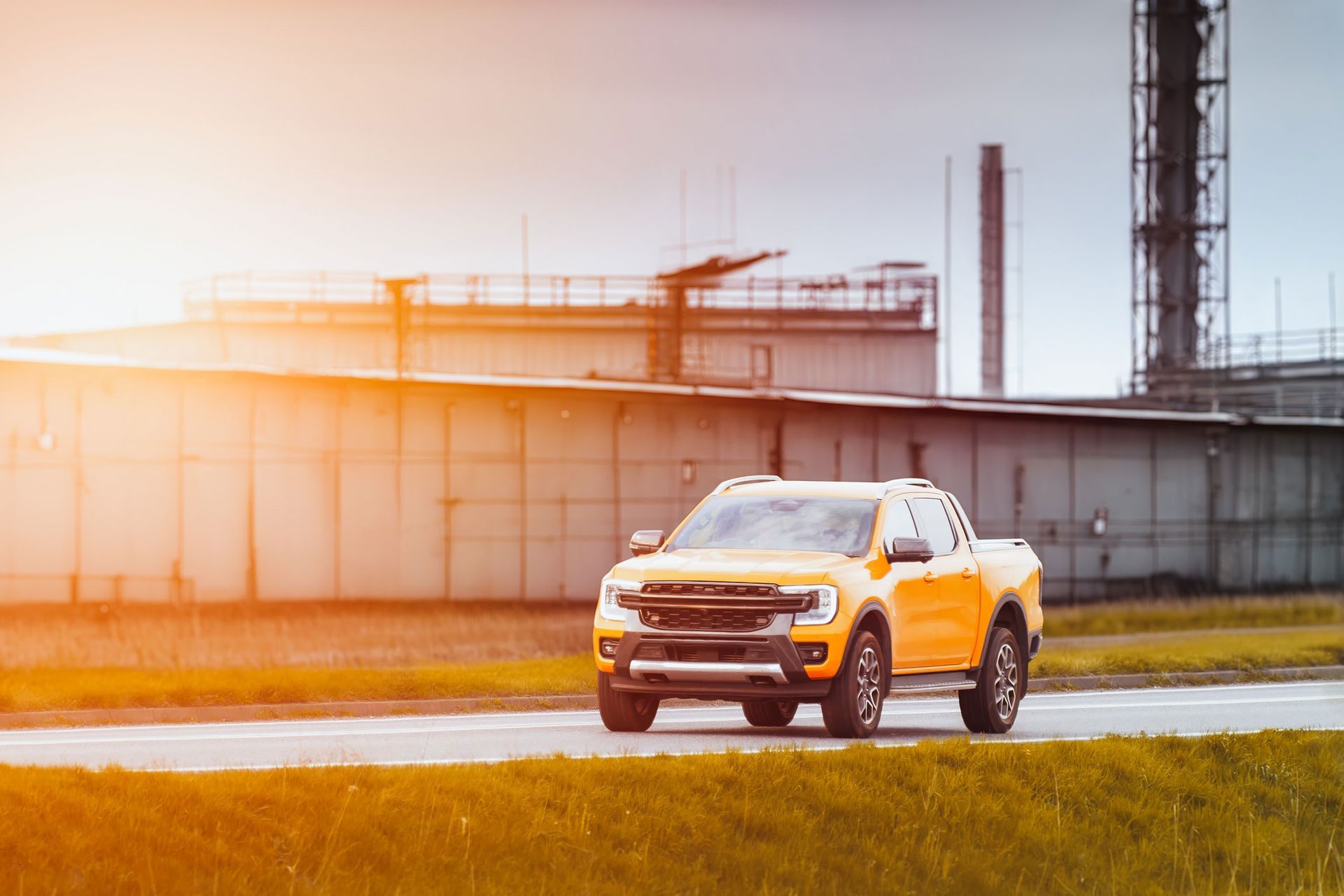 Yellow pickup truck driving on a road near industrial buildings in sunlight. Yellow pickup truck driving on a road near industrial buildings in sunlight.