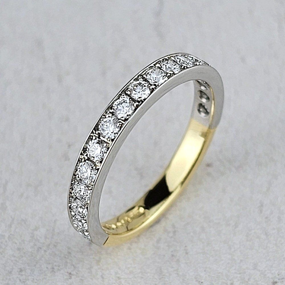A wedding ring with a platinum top, set with diamonds, on a yellow gold band.