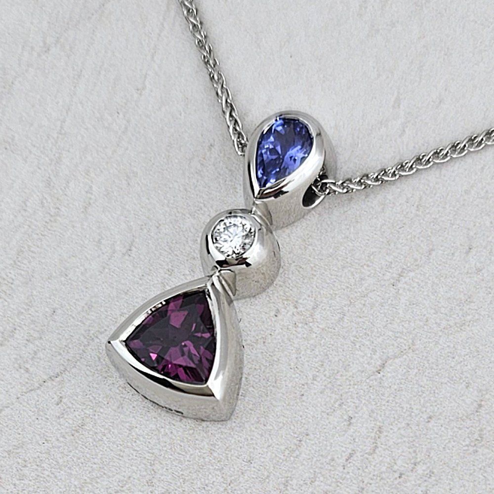 A birthstone pendant with a Tanzanite, a diamond, and a garnet