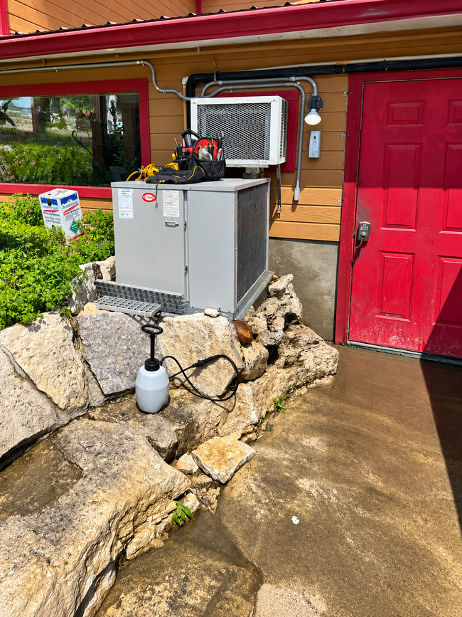 Outdoor utility area with gray equipment beside a red door and stone wall, on a wet concrete walkway
