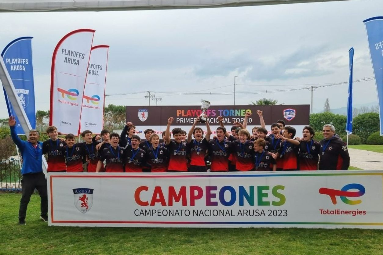Equipo de fútbol juvenil celebrando la victoria del campeonato, sosteniendo un trofeo y una pancarta que dice 