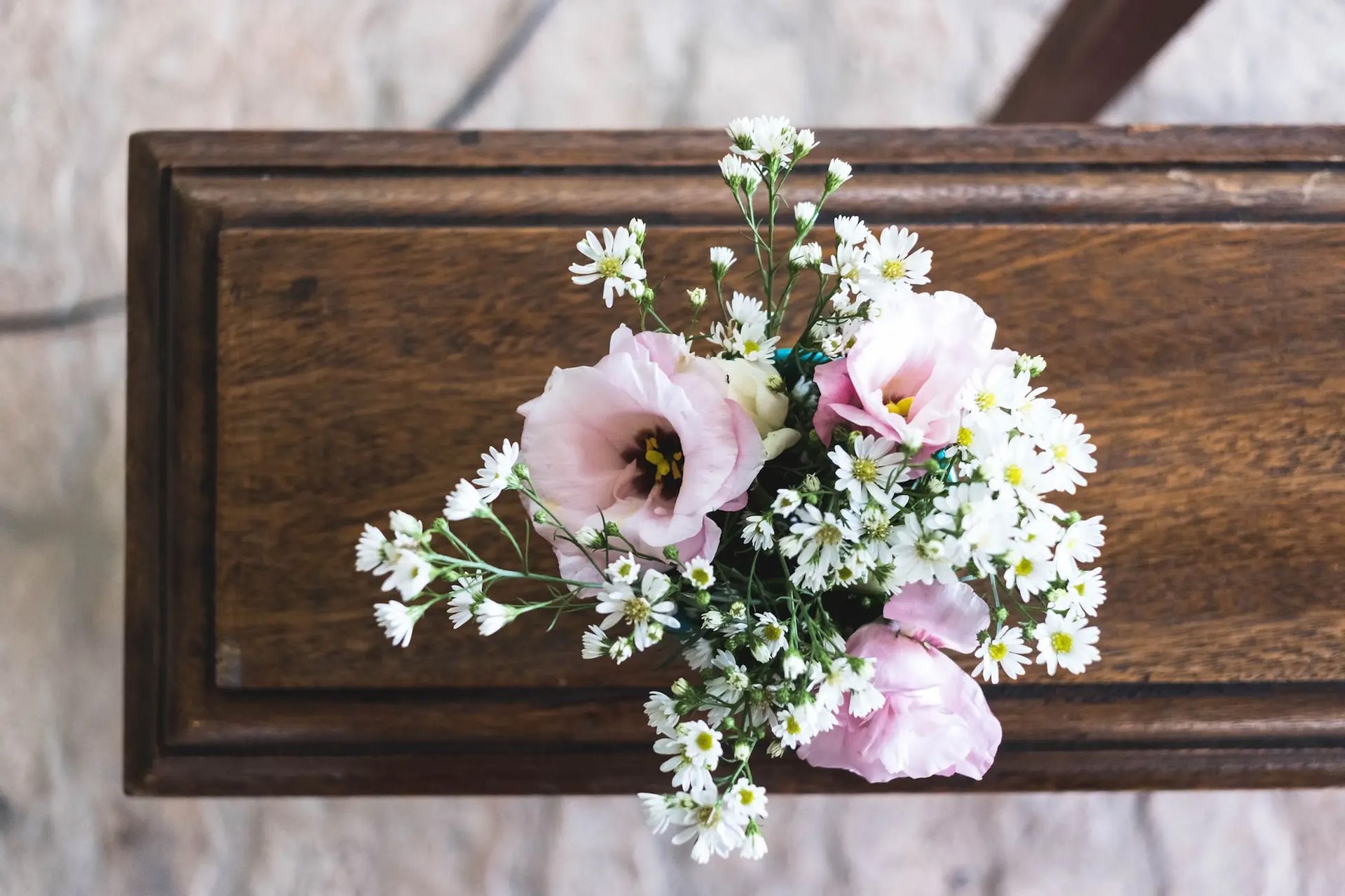 Wooden casket with a small bouquet of pink and white flowers on top.