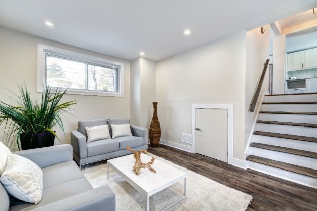 Cozy basement living room with gray couches, white table, and stairs leading upwards.