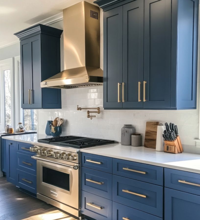 Blue kitchen cabinets with gold hardware, stainless steel appliances, white countertops.