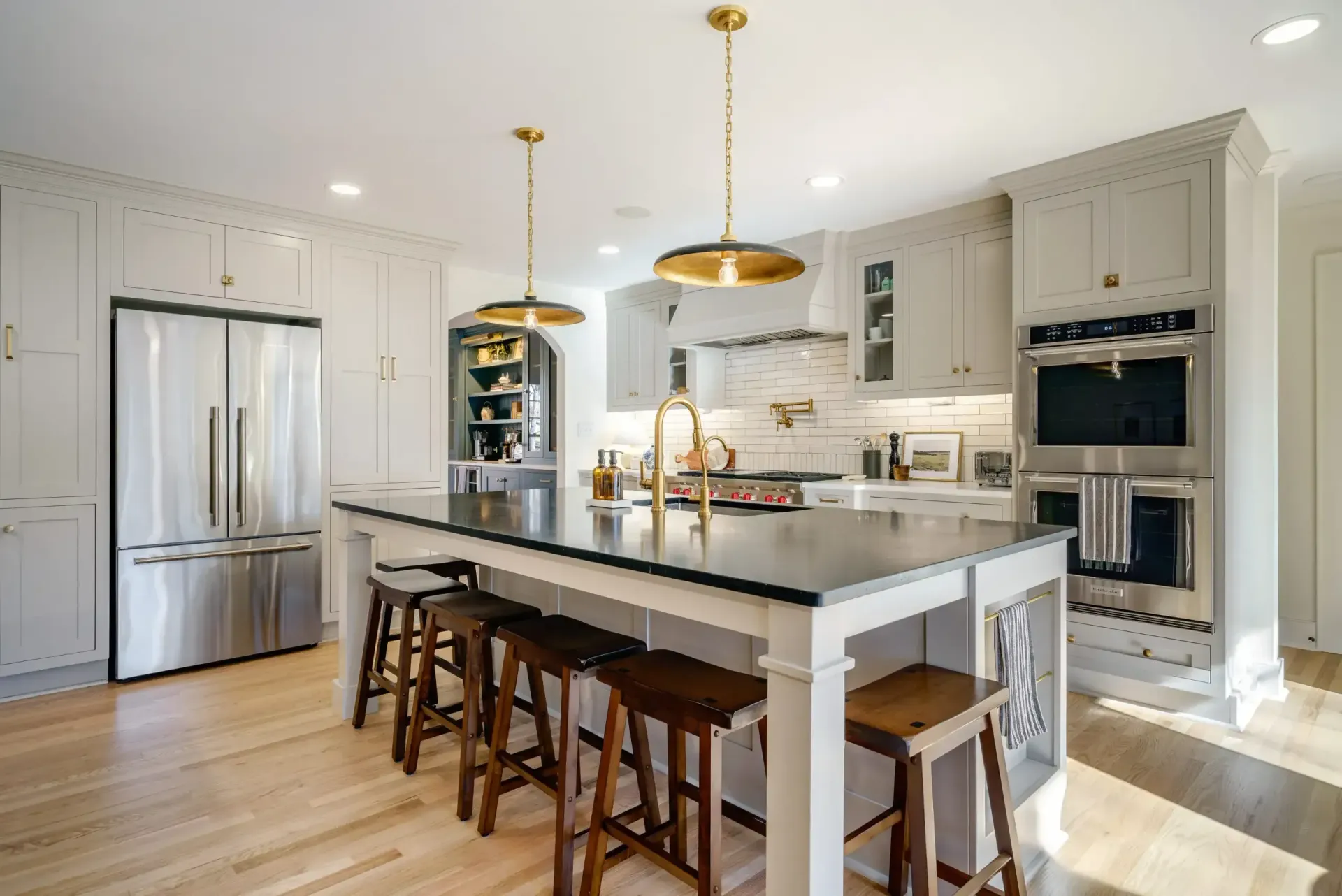 Modern kitchen with large island, stainless steel appliances, light wood floor, and gold accents.