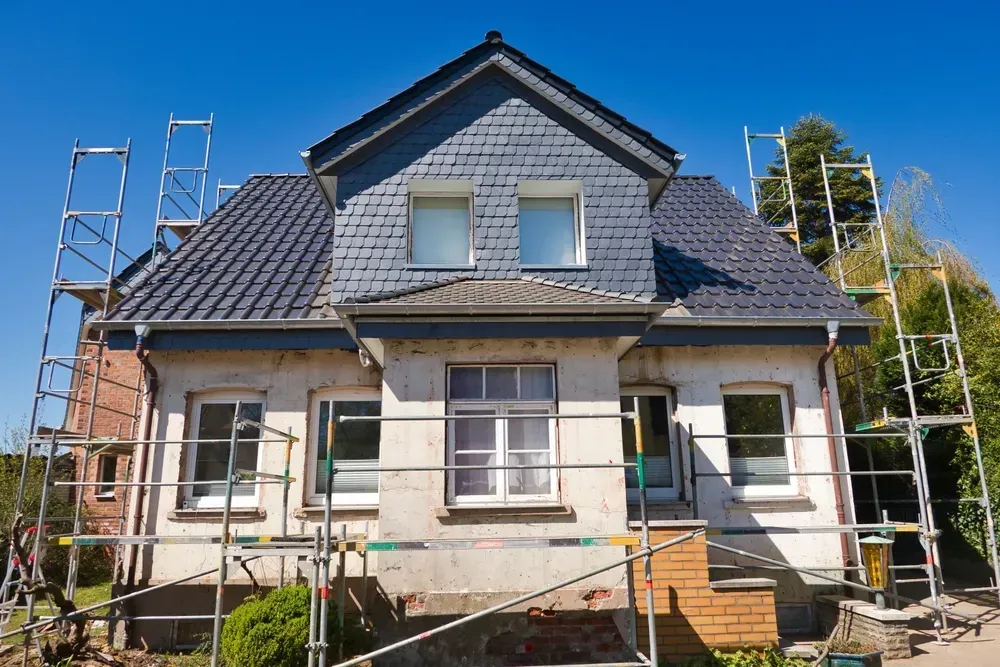 House under renovation with scaffolding, blue roof, and brick accents.