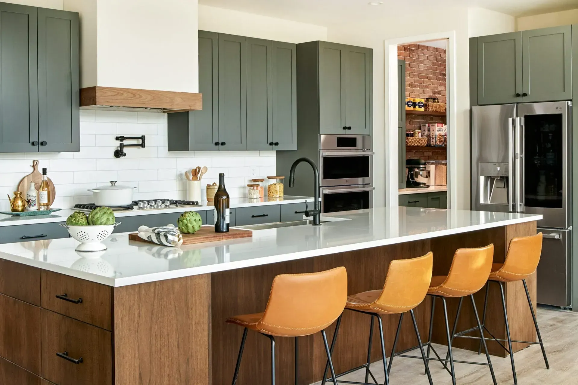Modern kitchen with sage green cabinets, brown island, white countertops, and orange bar stools.