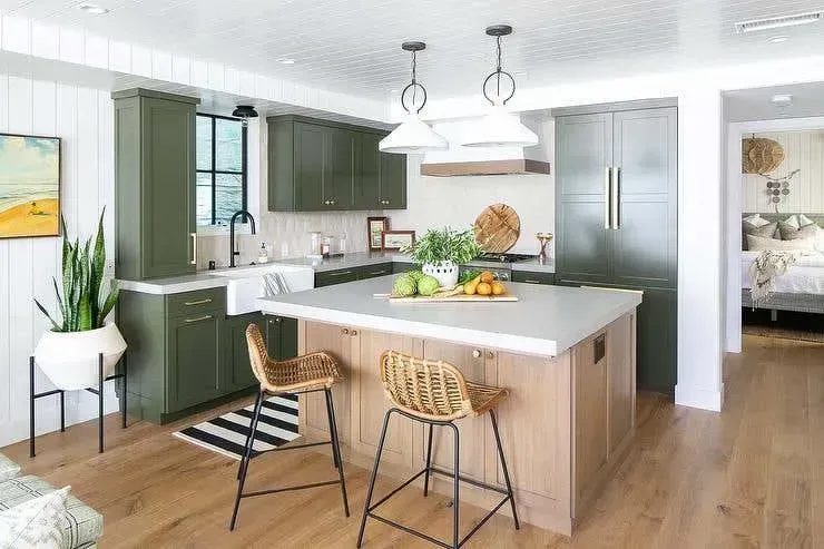 Modern kitchen with olive green cabinets, wooden island with white countertops, and wicker bar stools.