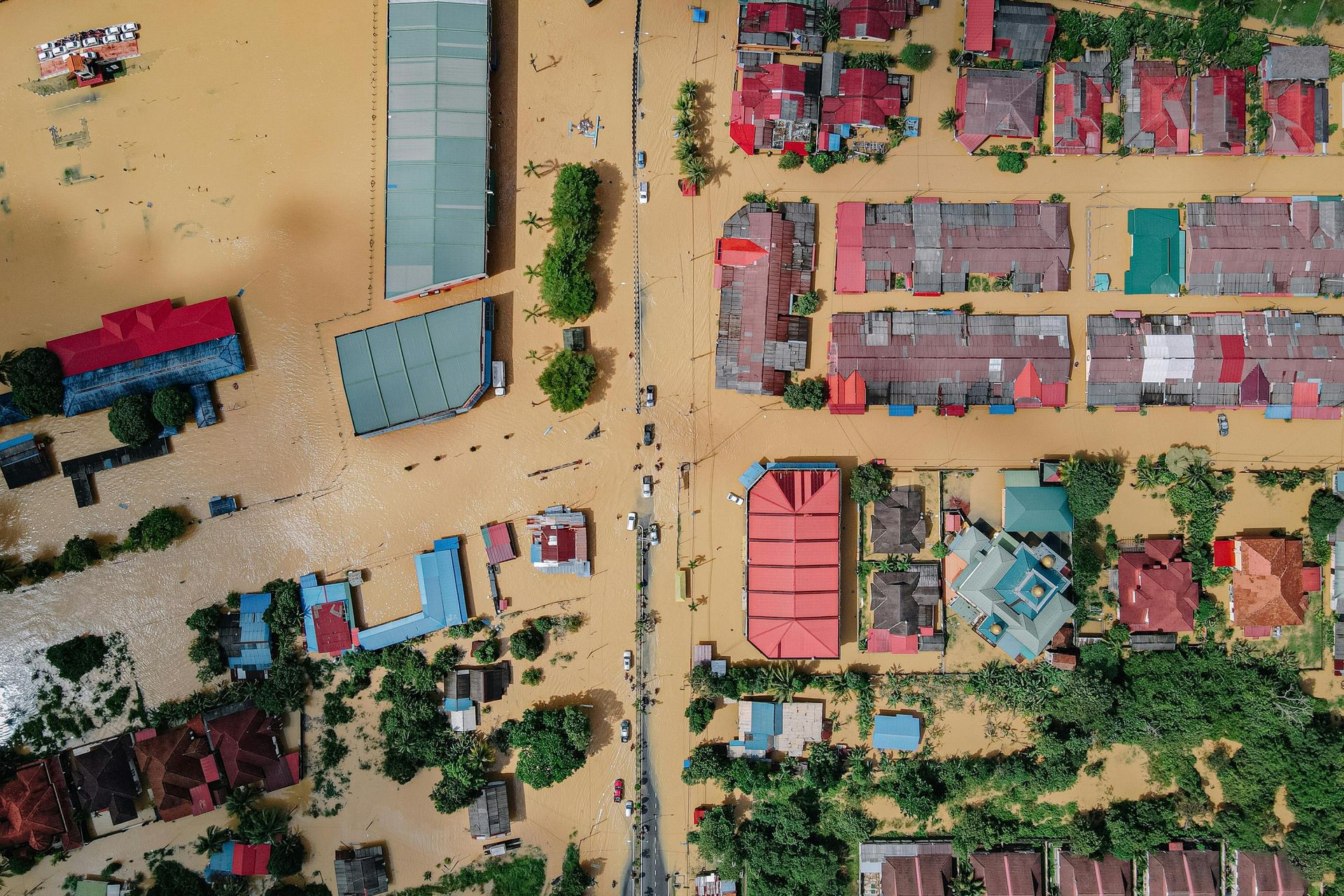Aerial view of a flooded town; houses and streets are submerged in brown water.