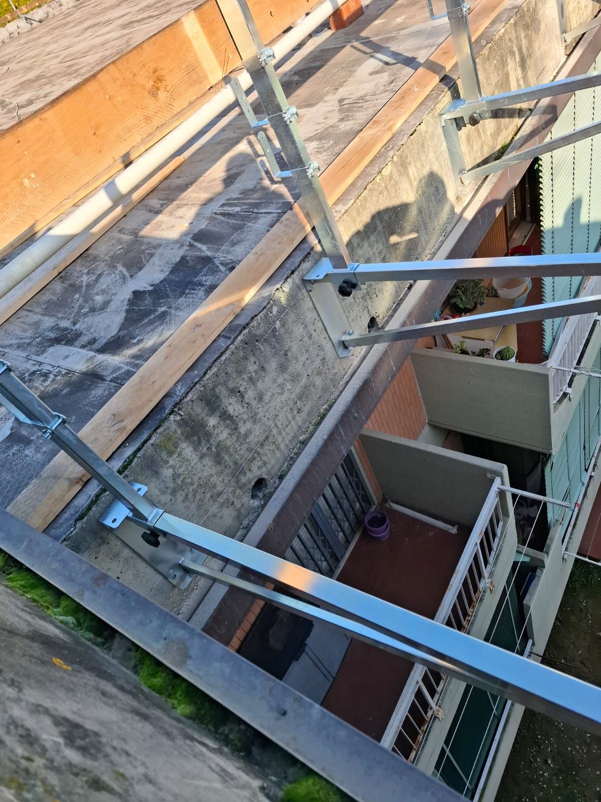 Passerella sul tetto con ringhiere metalliche accanto a un edificio in mattoni e cortile con scala a vista.