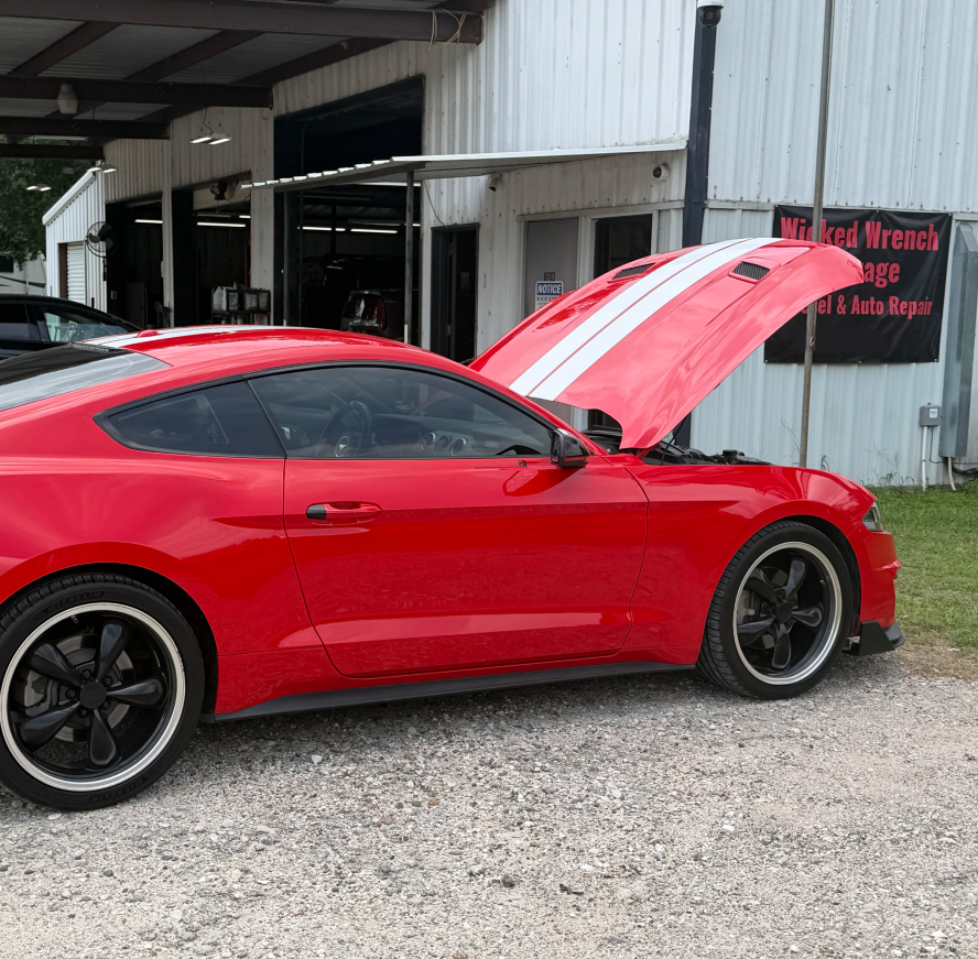 Red car with opened hood parked in front of The Wicked Wrench Garage in Conroe, TX