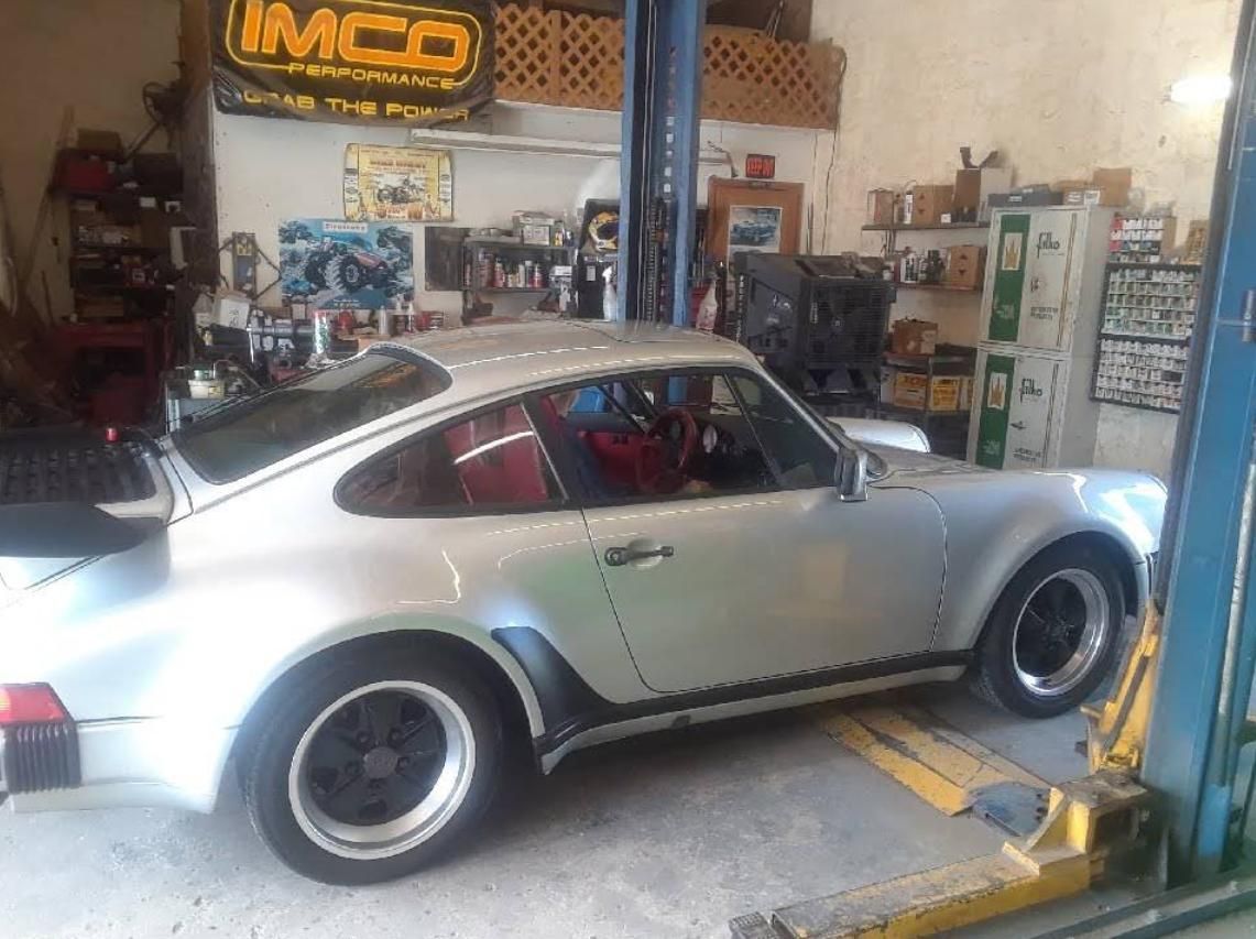 Silver classic Porsche 911 in an auto shop on a lift, with tools and equipment in the background.