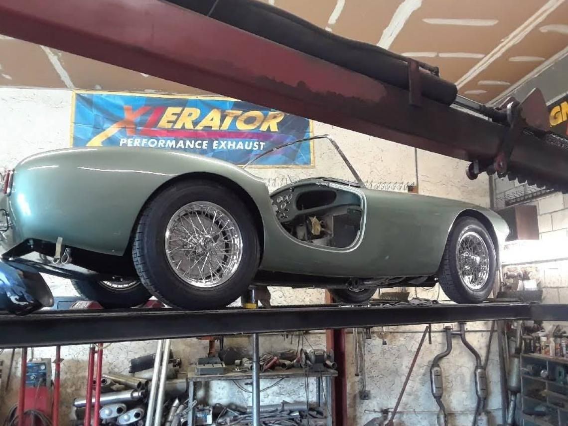 Classic silver race car displayed on a lift in an auto shop under a ZERATOR sign