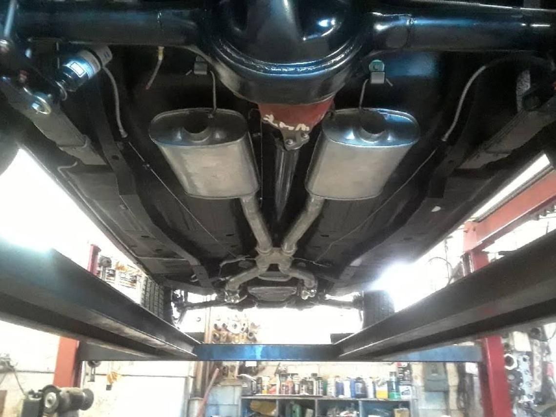 Underside of a car on a lift, showing dual exhaust pipes and suspension components.