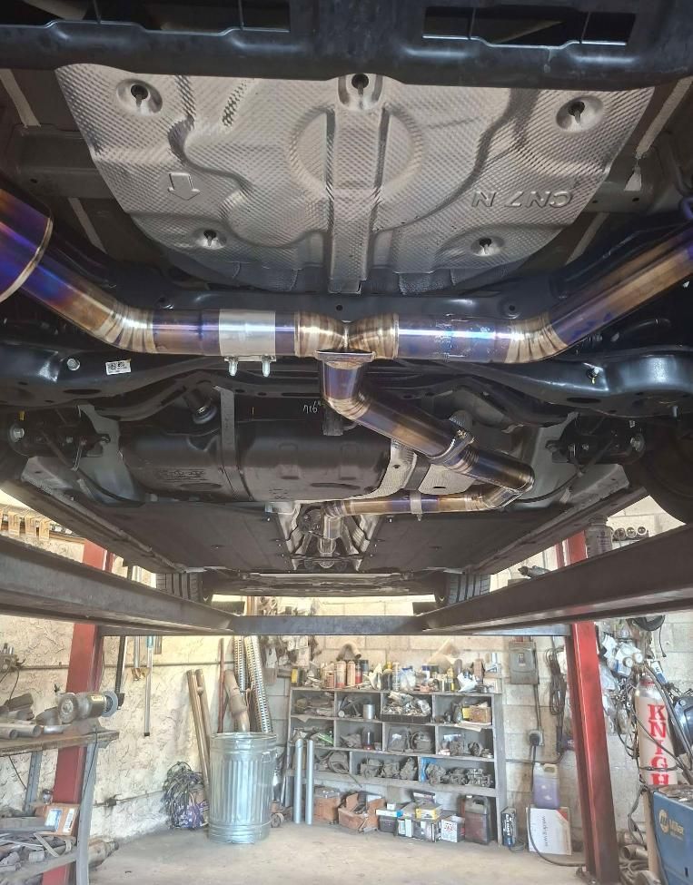 Undercarriage of a car on a lift in a garage, showing exhaust and chassis components.