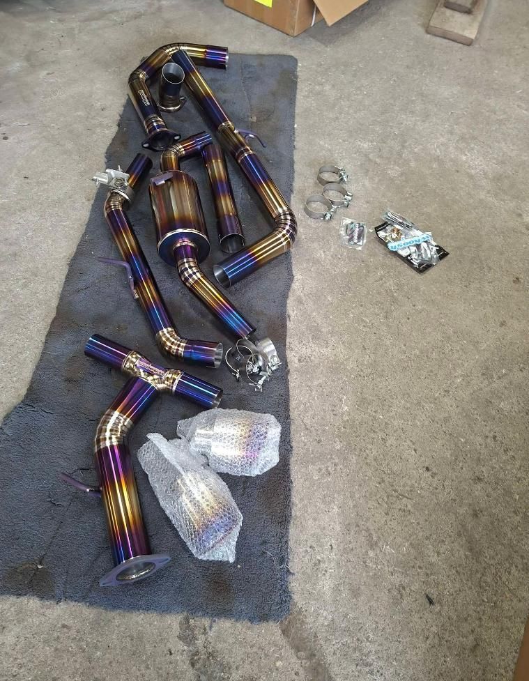 Colorful titanium exhaust pipe sections laid out on a concrete floor, with small hardware pieces nearby