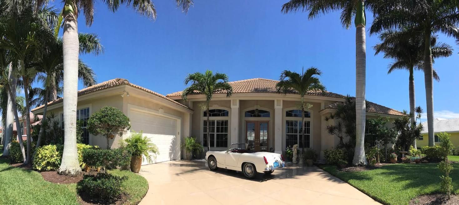 Luxury single-story house with a white convertible parked in the driveway and palm trees in front
