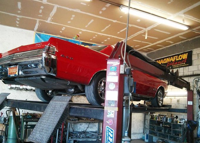 Red classic car lifted on an auto shop hoist inside a garage