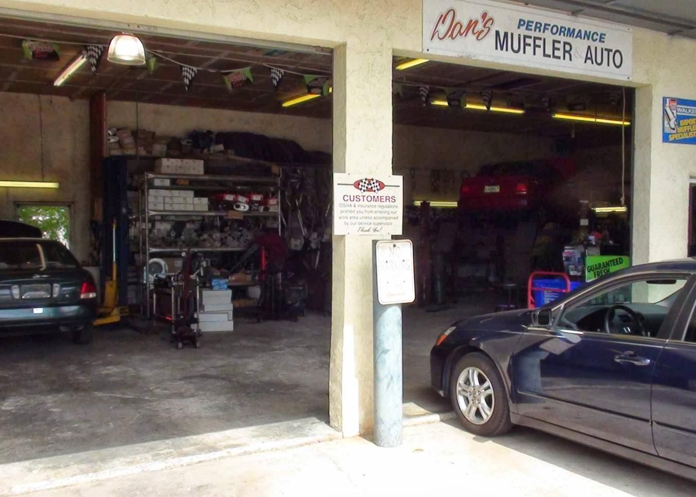 Auto repair shop garage with cars parked inside and outside, including a blue car at the entrance.
