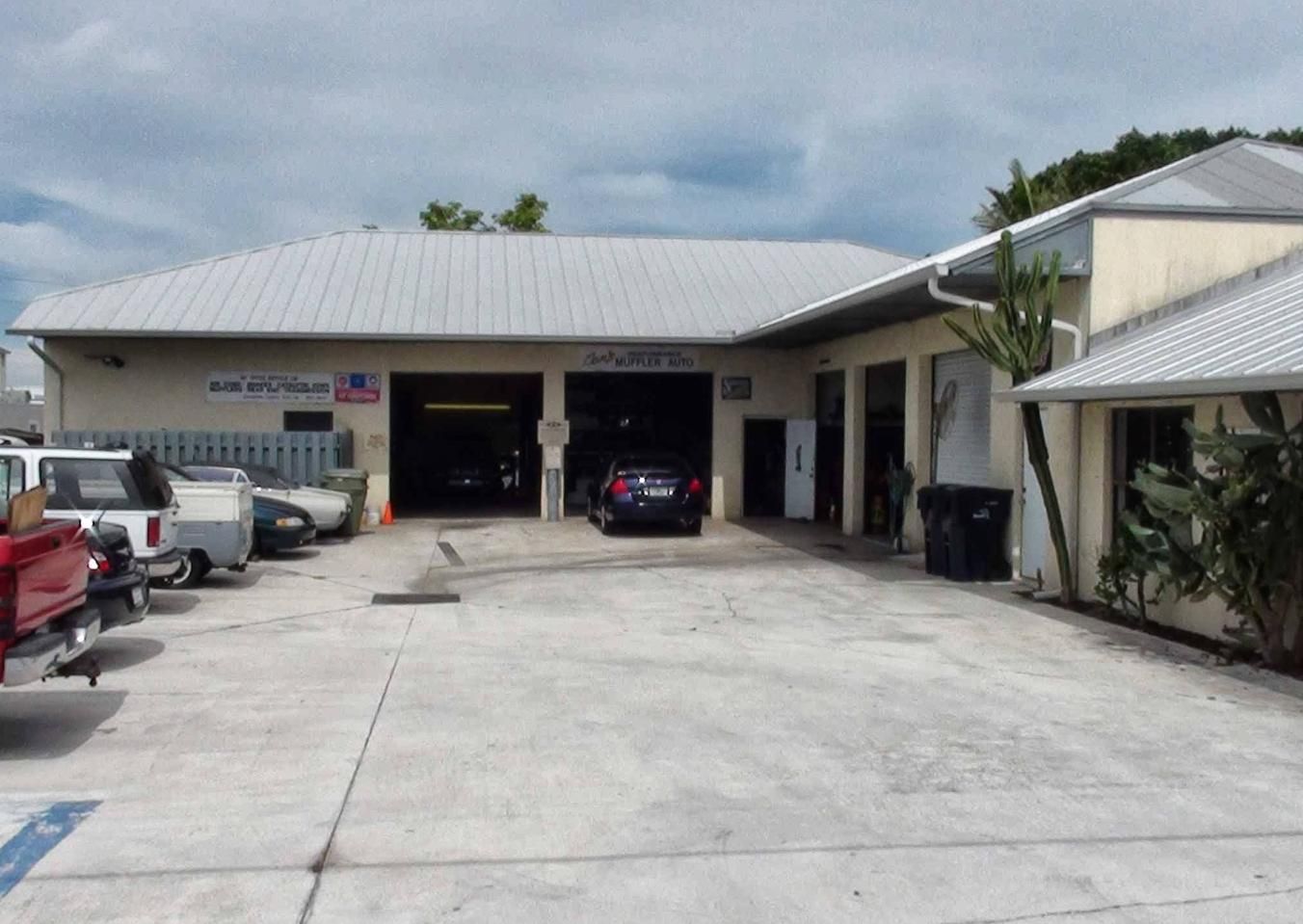 Parking lot of a small building with several parked cars and a covered entrance under a cloudy sky