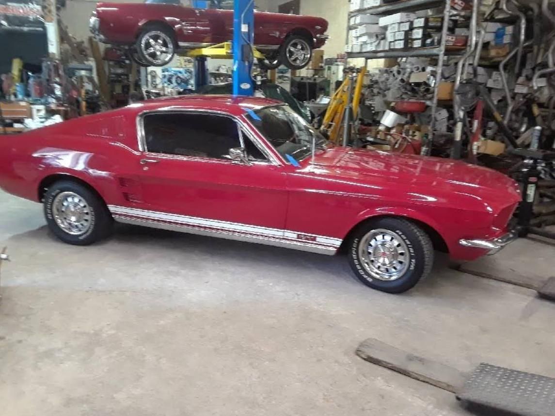 Red classic muscle car in a garage workshop, side view with chrome trim and polished wheels.