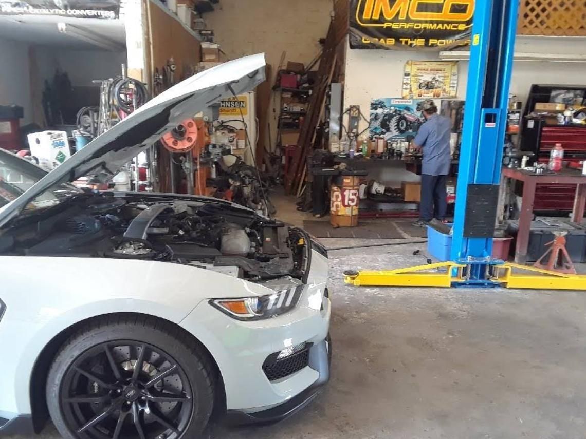 White car with hood open in an auto repair shop, near a blue lift and mechanic tools.