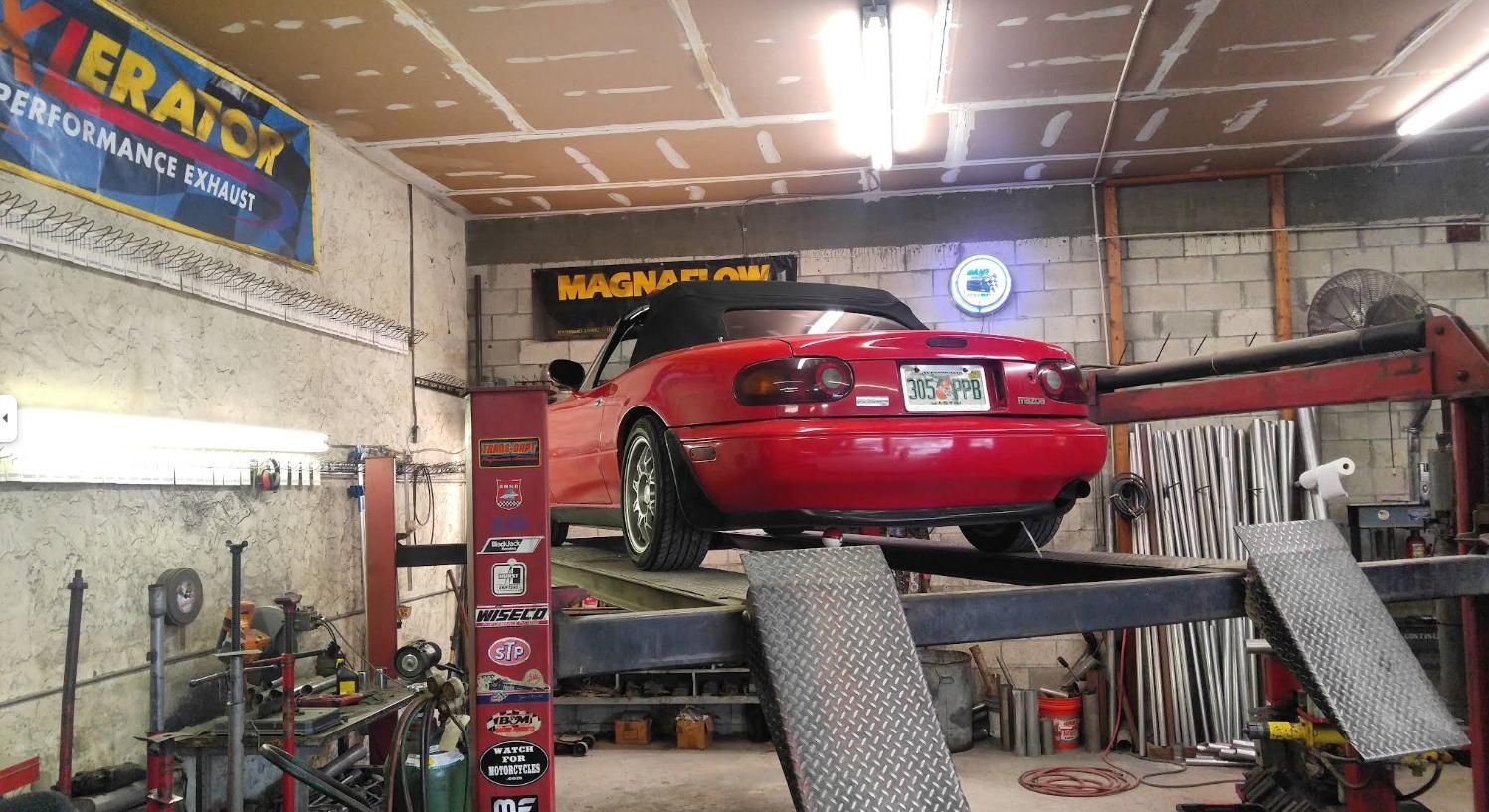 Red sports car on a lift inside an auto repair shop, rear view with ramps and tools nearby