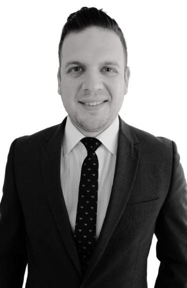 Black-and-white portrait of a smiling person in a suit, tie, and white shirt against a plain background.