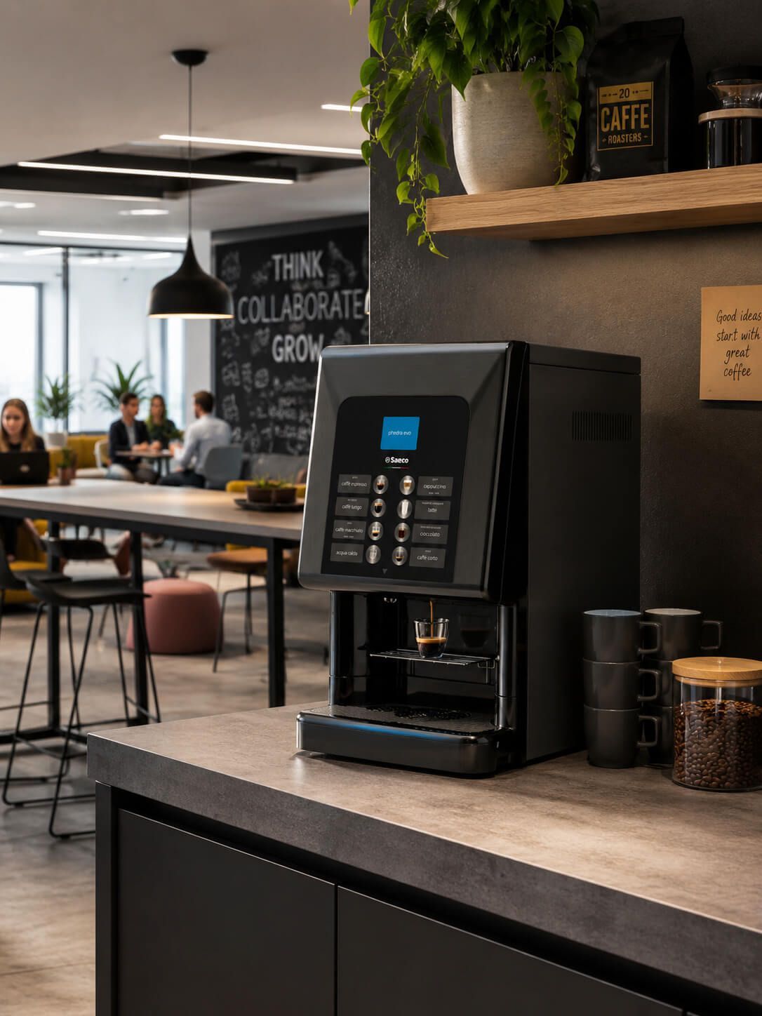 Máquina expendedora de café sobre una encimera en una moderna sala de descanso de oficina con mesas y lámparas colgantes.
