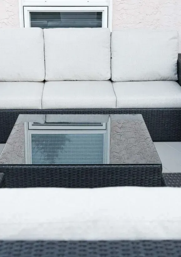 Outdoor patio with white-cushioned wicker seating, glass coffee table, and potted flowers