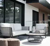White outdoor patio chairs around a black fire pit on a deck, with a green backyard and trees beyond.