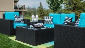 Outdoor patio with black wicker seating, turquoise cushions, and a glass-topped coffee table on green grass.