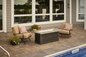 Patio seating area by a pool with two chairs, a coffee table, and potted flowers beside large windows