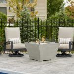 Modern patio seating with two white chairs and a square fire table on a stone terrace