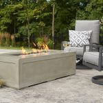 Modern patio with concrete fire pit, gray cushioned chair, and green trees in the background
