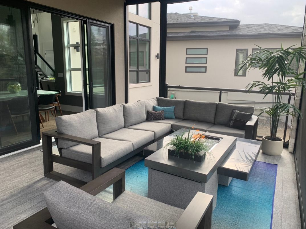Modern patio lounge with gray sectional seating, coffee table, and blue accent rug beside large windows