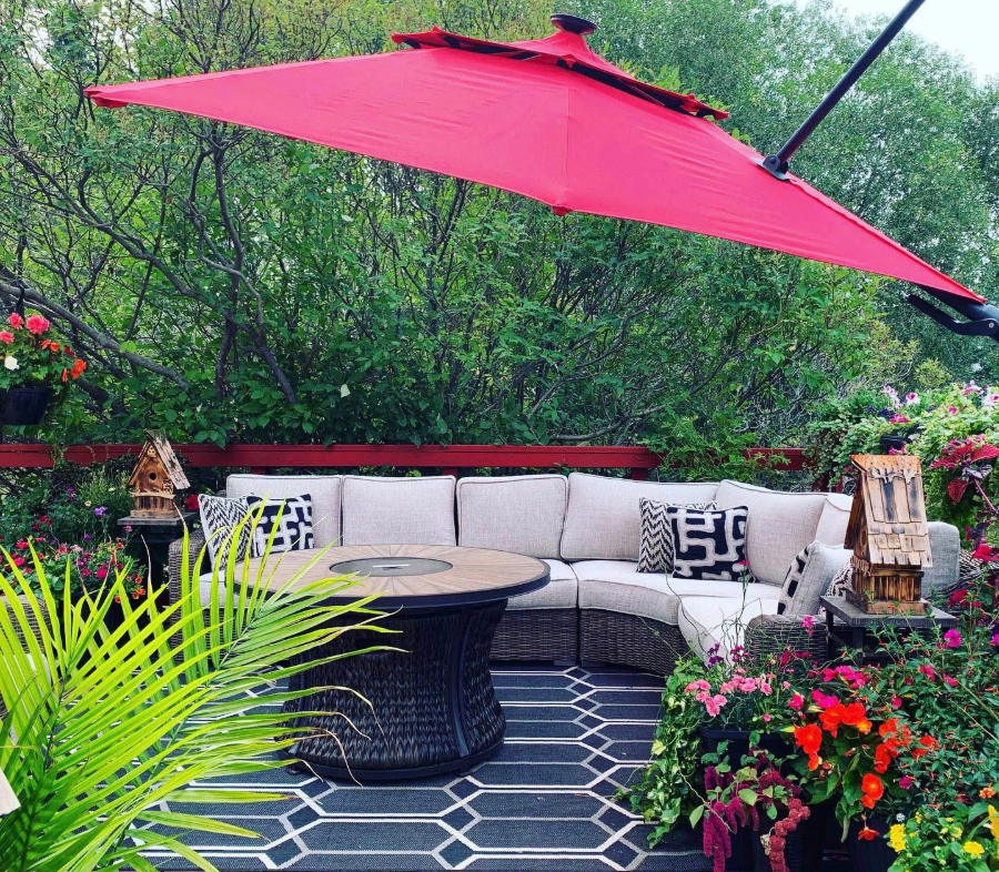 Patio lounge with beige sectional, round table, hot pink umbrella, and lush greenery
