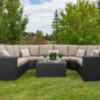 Outdoor wicker patio sectional with beige cushions, matching ottoman, and potted plants on a lawn