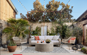 Cozy outdoor patio with white sofa, round fire pit table, potted plants, and string lights