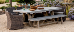 Outdoor dining table with wicker chairs and a wooden bench in a garden setting