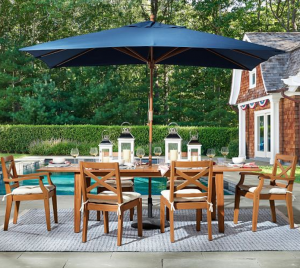 Outdoor patio dining set with wooden chairs, table, black umbrella, and lanterns by a pool.