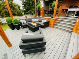 Modern patio with gray sectional, fire pit, black chairs, orange posts, and light wood deck steps