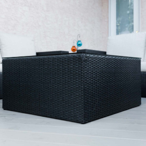 Black woven outdoor sectional sofa on a light patio with two small bottles on the back ledge