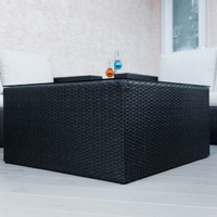 Black woven outdoor sectional sofa on a light patio with two small bottles on the back ledge