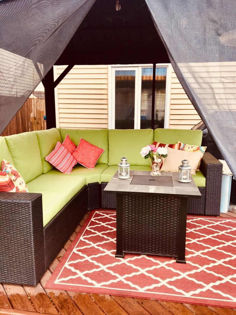 Outdoor patio lounge with lime green sectional, red rug, wicker table, and canopy shade