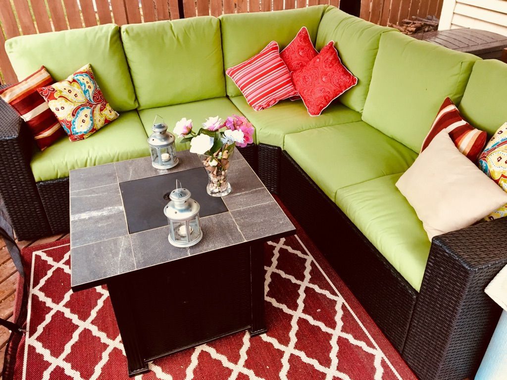 L-shaped patio sofa with green cushions, red pillows, and a black coffee table on a patterned red rug