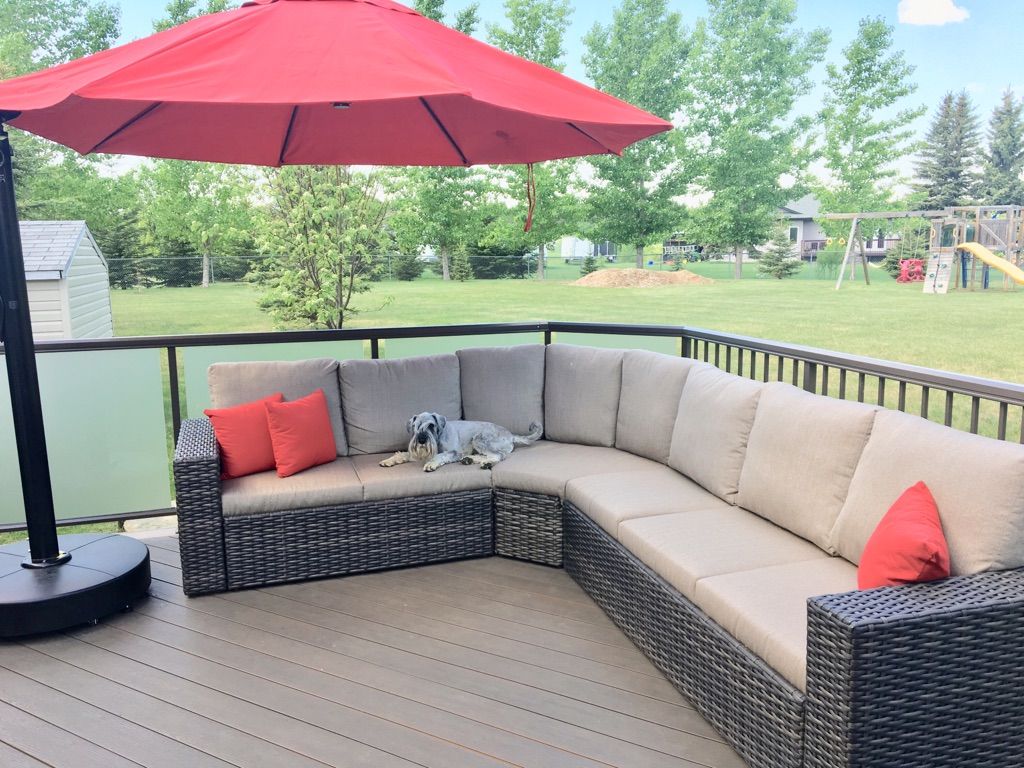 Patio deck with beige wicker sectional, red umbrella, and green backyard view